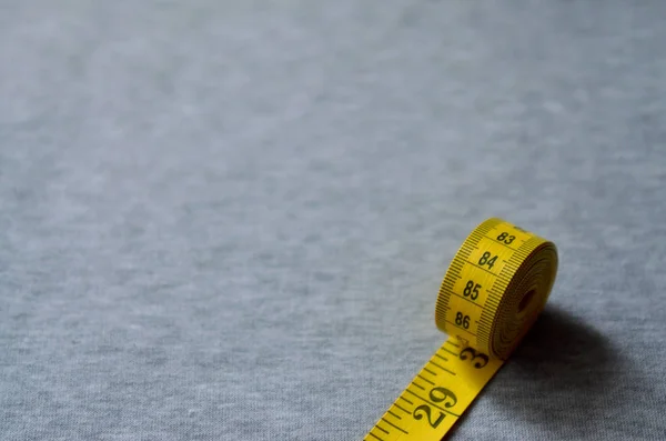 Желтая измерительная лента лежит на серой трикотажной ткани — стоковое фото