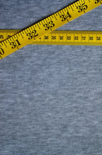 センチメートルまたはインチのフォームにおける数値指標と黄色の色の測定テープあるグレーのニット生地です 特定の身体サイズのミシン服の背景概念 — ストック写真