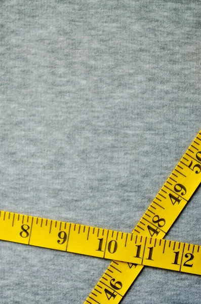 Желтая измерительная лента лежит на серой трикотажной ткани — стоковое фото