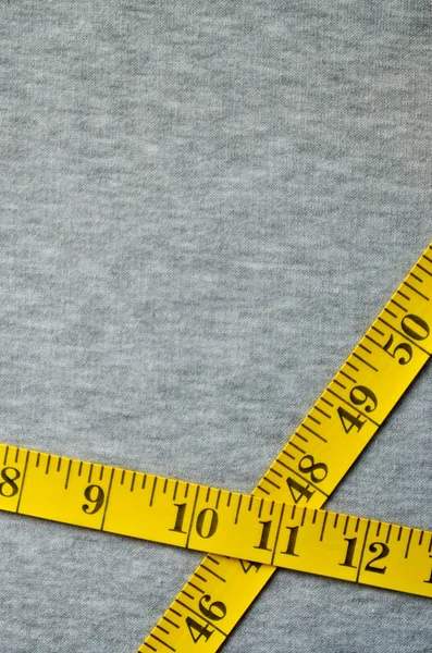 センチメートルまたはインチのフォームにおける数値指標と黄色の色の測定テープあるグレーのニット生地です 特定の身体サイズのミシン服の背景概念 — ストック写真