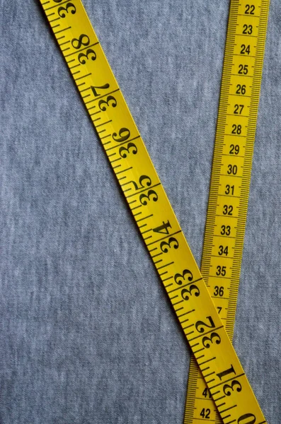 Κίτρινη ταινία μέτρησης βρίσκεται σε ένα γκρι πλεκτό ύφασμα — Φωτογραφία Αρχείου