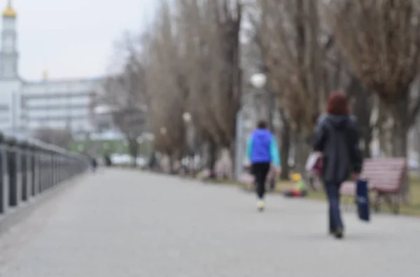 Blurred landscape of the spring park near the waterfront. Road ahead, decorated with trees and a low fence of the embankment