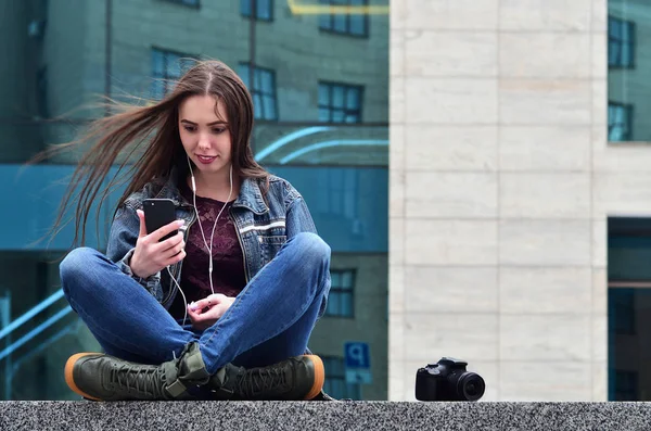 A girl photographer uses a smartphone and sits on a granite parapet