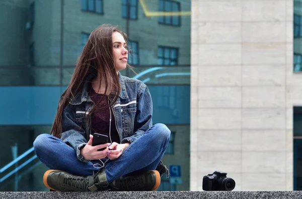 A girl photographer uses a smartphone and sits on a granite parapet