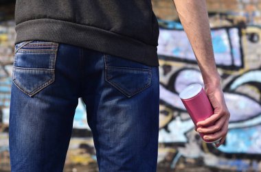 Mavi kirli kot ve gri kazak genç bir adamın eski bir tuğla duvar grafiti çizim boyalı arka planı elinde kullanılan boya sprey ile vücudun arka görünüm