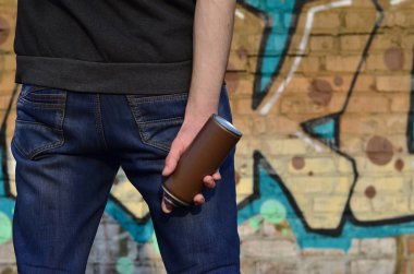 Mavi kirli kot ve gri kazak genç bir adamın eski bir tuğla duvar grafiti çizim boyalı arka planı elinde kullanılan boya sprey ile vücudun arka görünüm