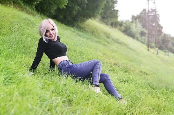 Retrato de uma jovem loira com cabelo curto sentado em um campo verde — Fotografia de Stock