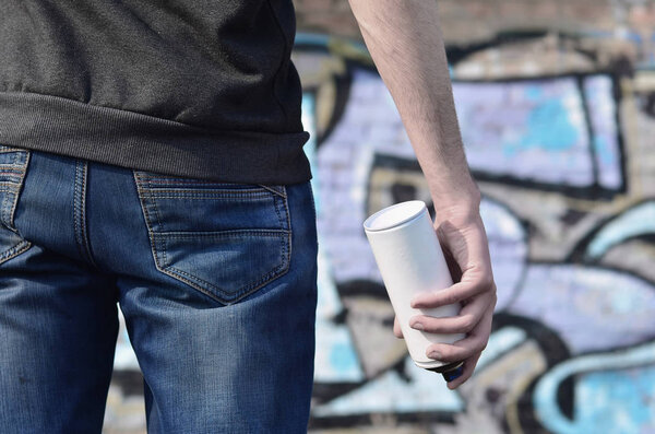 Фото хулигана, который портит государственную собственность, красит стены аэрозольной краской. Фрагмент тела молодого преступника с распылителем краски в грязной руке. Проблема повреждения имущества
