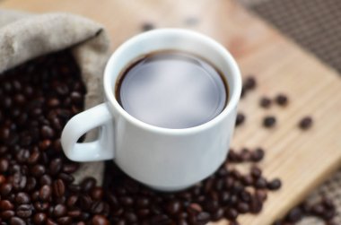 Kahverengi kahve çekirdekleri ve beyaz bir fincan sıcak kahve l tam bir çanta