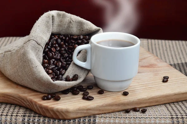 En full påse brun kaffebönor och en vit kopp hett kaffe l — Stockfoto