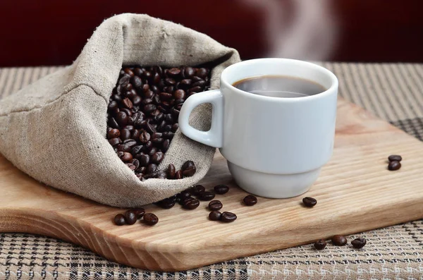 Un sac complet de grains de café marron et une tasse blanche de café chaud l — Photo