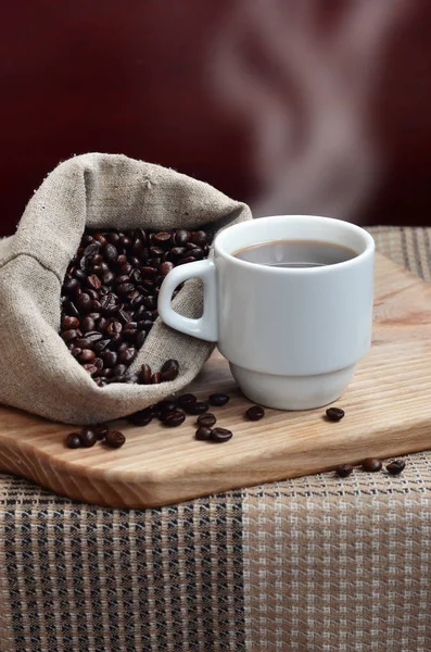 Un sac complet de grains de café marron et une tasse blanche de café chaud l — Photo