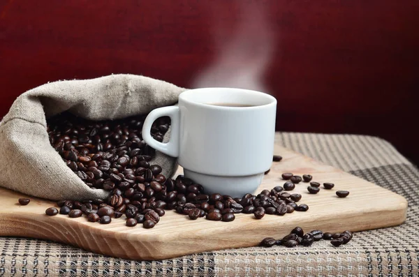 Un sac complet de grains de café marron et une tasse blanche de café chaud l — Photo