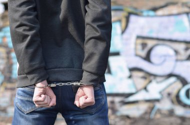 Arkadan Görünüm boyalı duvarlar arka planı gettosundan tutuklandı haydut. Suçlu gözaltına alındı ve elleri kelepçeli. Suç ile mücadele kavramı