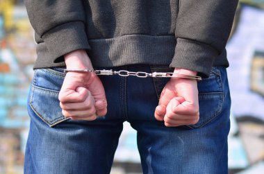 Arkadan Görünüm boyalı duvarlar arka planı gettosundan tutuklandı haydut. Suçlu gözaltına alındı ve elleri kelepçeli. Suç ile mücadele kavramı
