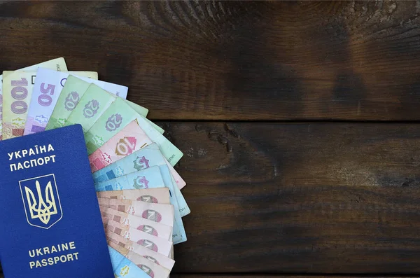 Uma fotografia de um passaporte ucraniano e uma certa quantidade de dinheiro ucraniano em uma superfície de madeira — Fotografia de Stock