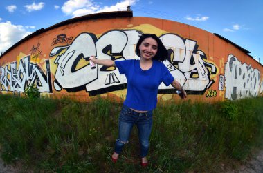 Siyah saçlı ve piercing ile duygusal bir genç kız portresi. Sprey boya... kutularını graffiti duvar arka plan üzerinde elinde bir kızla bir geniş açı fotoğraf. Bir balıkgözü lens modern bir portresi