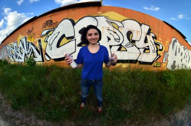 Siyah saçlı ve piercing ile duygusal bir genç kız portresi. Sprey boya... kutularını graffiti duvar arka plan üzerinde elinde bir kızla bir geniş açı fotoğraf. Bir balıkgözü lens modern bir portresi