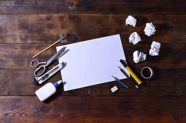 A school or office still life with a white blank sheet of paper and many office supplies. The school supplies lie on a brown wooden background. Place for text