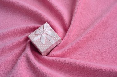 Bir küçük hediye kutusu pembe küçük bir yay ile yumuşak ve tüylü hafif pembe Polar kumaş bir battaniye var bir sürü kabartma kıvrımları ile yatıyor. Güzel kız için bir hediye için ambalaj