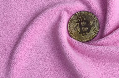 Altın bitcoin yumuşak ve kabarık hafif pembe Polar kumaş çok sayıda kabartma kıvrımları ile yapılmış bir battaniye yatıyor. Kıvrımları şeklinde bir ekran kartı soğutucu fan benzer