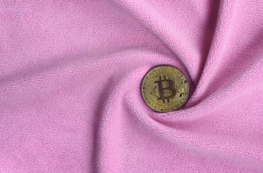 Altın bitcoin yumuşak ve kabarık hafif pembe Polar kumaş çok sayıda kabartma kıvrımları ile yapılmış bir battaniye yatıyor. Kıvrımları şeklinde bir ekran kartı soğutucu fan benzer