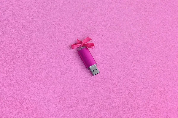 Brilliant pink usb flash memory card with a pink bow lies on a blanket of soft and furry light pink fleece fabric. Classic female gift design for a memory card