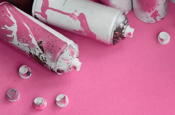 Some used pink aerosol spray cans and nozzles with paint drips lies on a blanket of soft and furry light pink fleece fabric. Classic female design color. Graffiti hooliganism concept