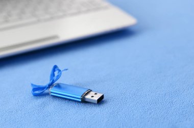 Parlak mavi usb flash bellek kart mavi bir yay ile yumuşak ve tüylü ışık mavi Polar kumaş beyaz bir dizüstü bilgisayar için bir battaniye yatıyor. Klasik kadın hediye tasarım a bellek oyun kağıdı için