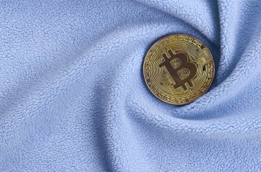 Altın bitcoin yumuşak ve kabarık ışık mavi Polar kumaş çok sayıda kabartma kıvrımları ile yapılmış bir battaniye yatıyor. Kıvrımları şeklinde bir ekran kartı soğutucu fan benzer