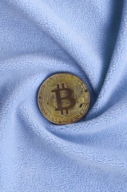 Altın bitcoin yumuşak ve kabarık ışık mavi Polar kumaş çok sayıda kabartma kıvrımları ile yapılmış bir battaniye yatıyor. Kıvrımları şeklinde bir ekran kartı soğutucu fan benzer