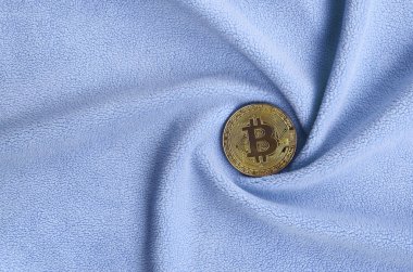 Altın bitcoin yumuşak ve kabarık ışık mavi Polar kumaş çok sayıda kabartma kıvrımları ile yapılmış bir battaniye yatıyor. Kıvrımları şeklinde bir ekran kartı soğutucu fan benzer