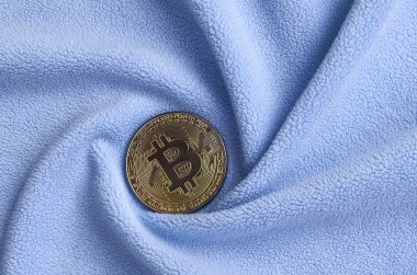 Altın bitcoin yumuşak ve kabarık ışık mavi Polar kumaş çok sayıda kabartma kıvrımları ile yapılmış bir battaniye yatıyor. Kıvrımları şeklinde bir ekran kartı soğutucu fan benzer