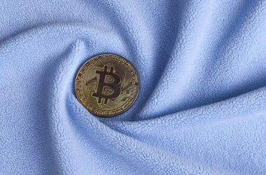 Altın bitcoin yumuşak ve kabarık ışık mavi Polar kumaş çok sayıda kabartma kıvrımları ile yapılmış bir battaniye yatıyor. Kıvrımları şeklinde bir ekran kartı soğutucu fan benzer