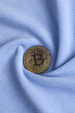 Altın bitcoin yumuşak ve kabarık ışık mavi Polar kumaş çok sayıda kabartma kıvrımları ile yapılmış bir battaniye yatıyor. Kıvrımları şeklinde bir ekran kartı soğutucu fan benzer