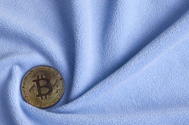 Altın bitcoin yumuşak ve kabarık ışık mavi Polar kumaş çok sayıda kabartma kıvrımları ile yapılmış bir battaniye yatıyor. Kıvrımları şeklinde bir ekran kartı soğutucu fan benzer