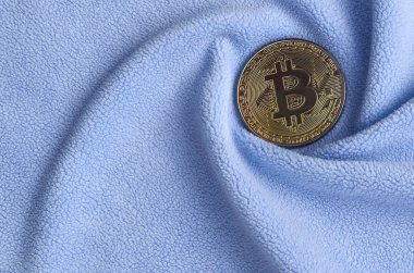 Altın bitcoin yumuşak ve kabarık ışık mavi Polar kumaş çok sayıda kabartma kıvrımları ile yapılmış bir battaniye yatıyor. Kıvrımları şeklinde bir ekran kartı soğutucu fan benzer