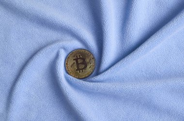 Altın bitcoin yumuşak ve kabarık ışık mavi Polar kumaş çok sayıda kabartma kıvrımları ile yapılmış bir battaniye yatıyor. Kıvrımları şeklinde bir ekran kartı soğutucu fan benzer