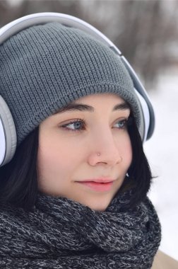 Oldukça çekici beyaz gözlü kız hipster kış park portresi. Kulaklıklar üzerinde müzik dinliyor. Gençlik sokak moda. Kış eğlence.