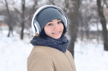 Pretty genç kız giyim sıcak kış etkilidirler ve eşarp. Soğuk havalarda kulaklık ile eğlenceli esmer kadın modeli yürümek dışında. Mutlu model poz gülümseyerek. İyi tatiller hava