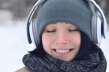 Oldukça çekici beyaz gözlü kız hipster kış park portresi. Kulaklıklar üzerinde müzik dinliyor. Gençlik sokak moda. Kış eğlence.
