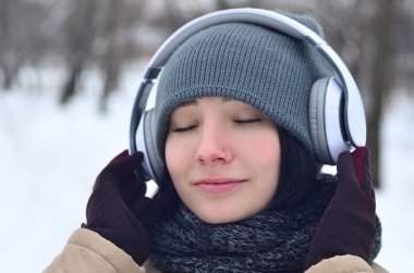 Güzellik kız kış orman içinde. Güzel genç esmer beyaz kadın şık kahverengi ceket ve sıcak siyah eşarp büyük beyaz kulaklık ile müzik dinlemek deldi.