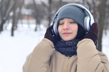 Oldukça çekici beyaz gözlü kız hipster kış park portresi. Kulaklıklar üzerinde müzik dinliyor. Gençlik sokak moda. Kış eğlence.