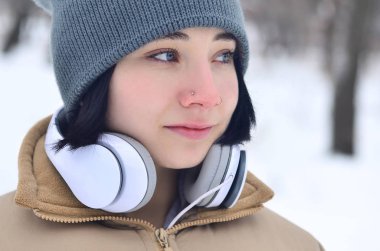Oldukça çekici beyaz gözlü kız hipster kış park portresi. Kulaklıklar üzerinde müzik dinliyor. Gençlik sokak moda. Kış eğlence.