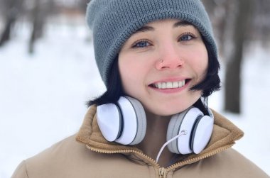 Pretty genç kız giyim sıcak kış etkilidirler ve eşarp. Soğuk havalarda kulaklık ile eğlenceli esmer kadın modeli yürümek dışında. Mutlu model poz gülümseyerek. İyi tatiller hava