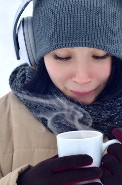 Karlı ahşap oldukça çekici beyaz gözlü kız kış portresi. O onun elinde kahve fincanı büyük beyaz kulaklık müzik dinliyor. Açık havada yürüyüşler