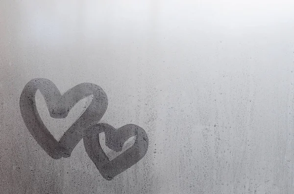 Couple of abstract blurred love heart symbol drawn by hand on the wet window glass with sunlight background. Template for Valentine Day postcards