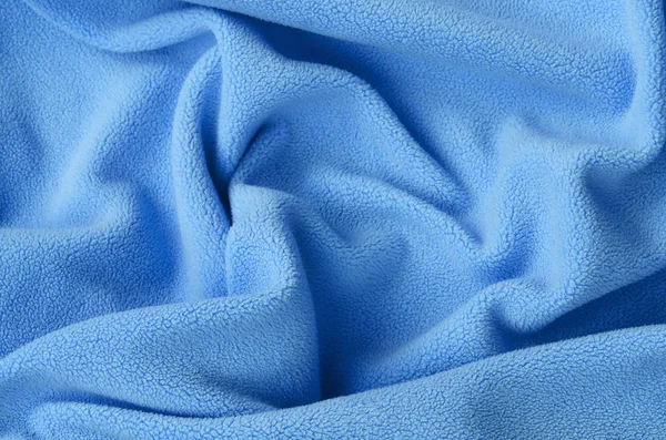 The blanket of furry blue fleece fabric. A background of light blue soft plush fleece material with a lot of relief folds