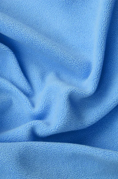 The blanket of furry blue fleece fabric. A background of light blue soft plush fleece material with a lot of relief folds