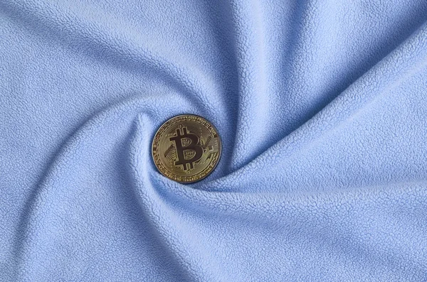 Altın bitcoin yumuşak ve kabarık ışık mavi Polar kumaş çok sayıda kabartma kıvrımları ile yapılmış bir battaniye yatıyor. Kıvrımları şeklinde bir ekran kartı soğutucu fan benzer